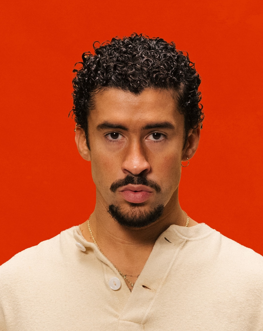 Prévu en concert à Paris et Marseille en 2026, le chanteur Bad Bunny prend la pose sur un fond rouge.